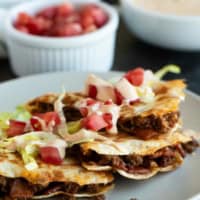 Bacon Cheeseburger Quesadillas cut into triangles and served with lettuce, tomatoes, and special sauce.