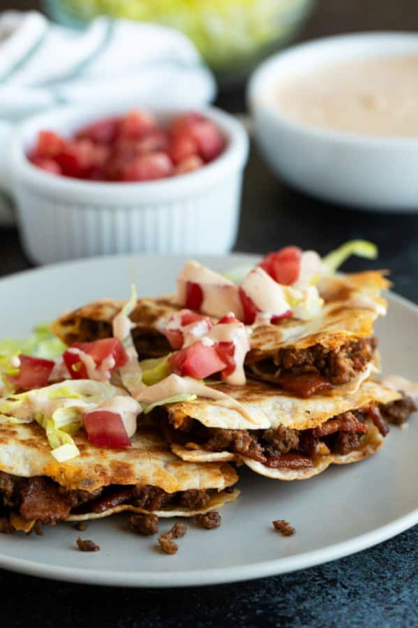 Bacon Cheeseburger Quesadillas cut into triangles and served with lettuce, tomatoes, and special sauce.