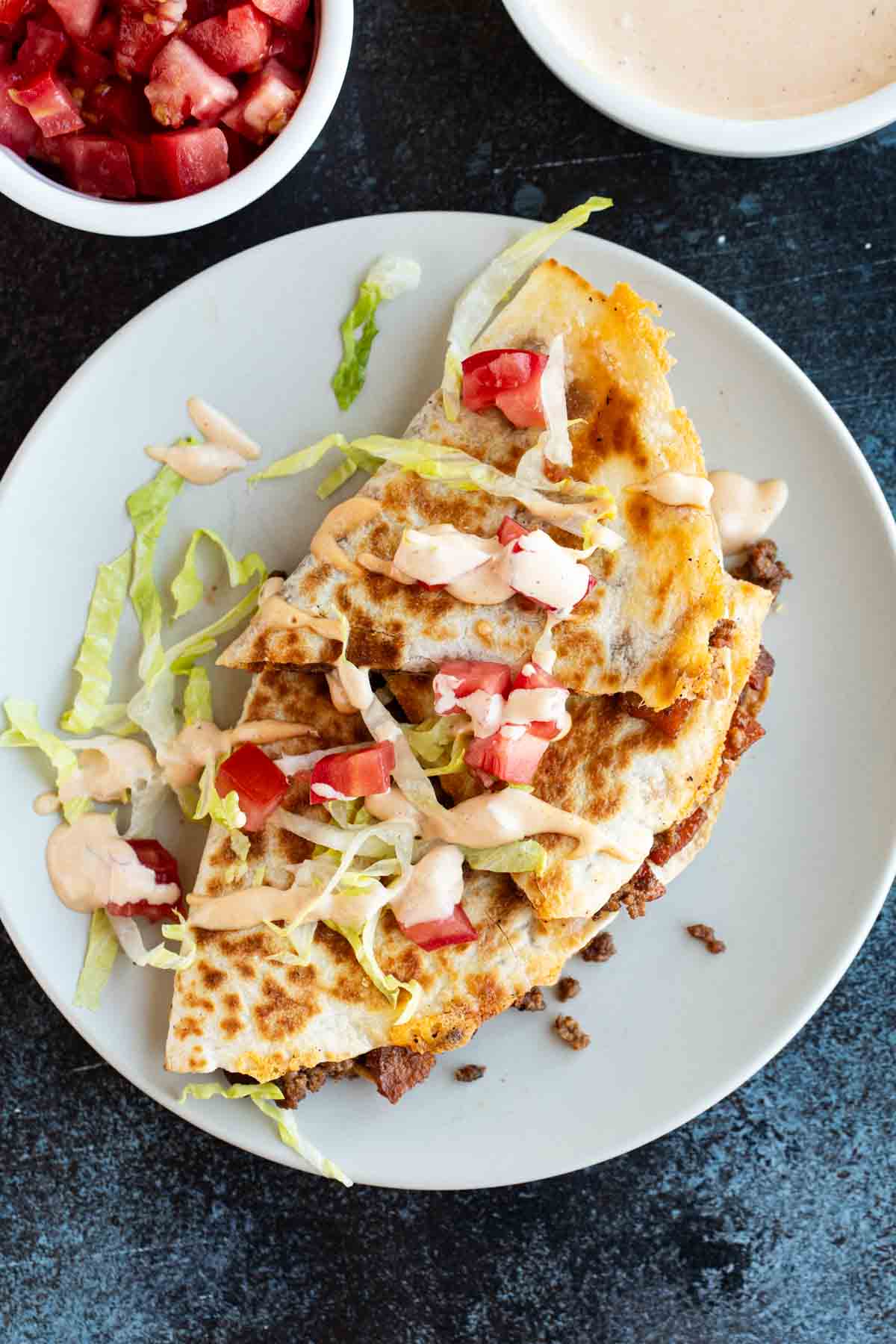 Bacon Cheeseburger Quesadilla on a plate topped with lettuce, tomato, and special sauce.