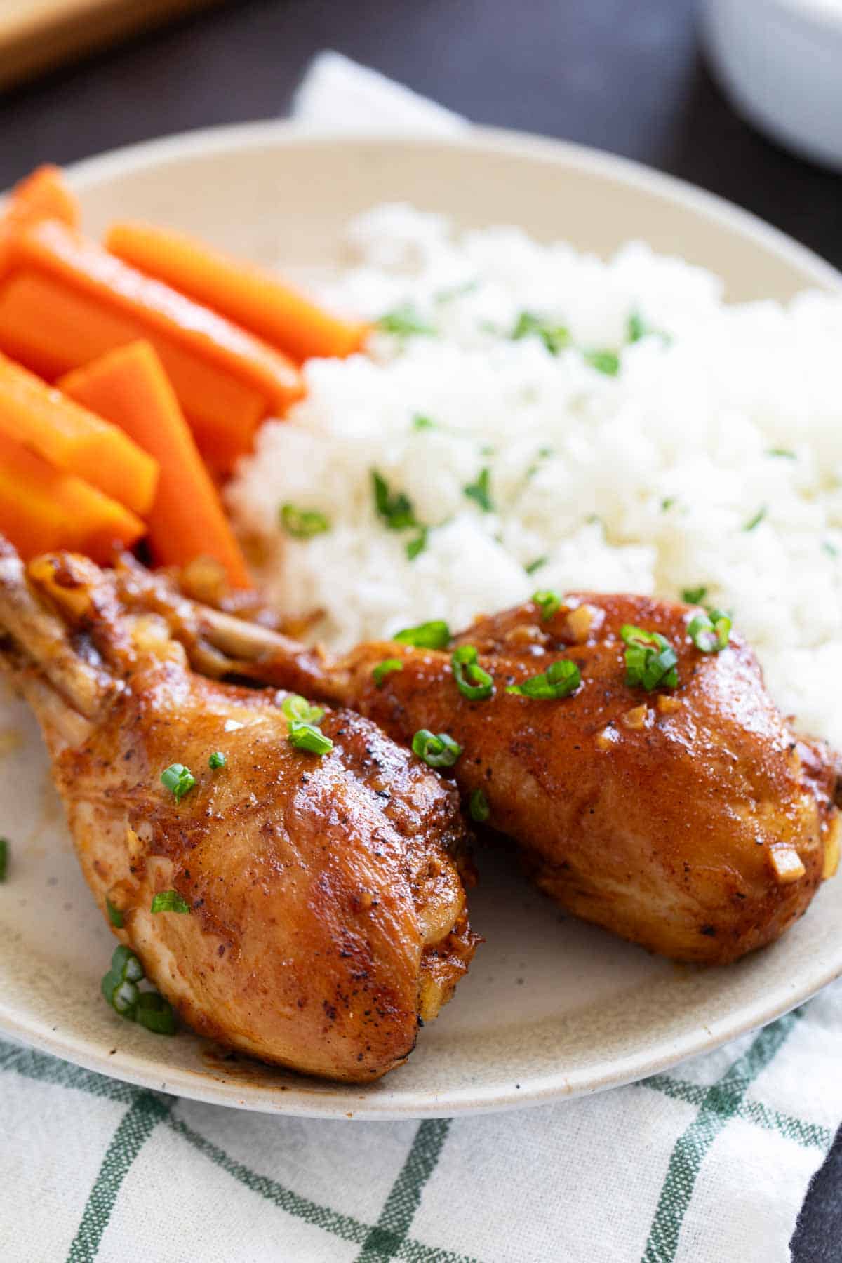 Two Honey Balsamic Chicken Drumsticks on a plate with carrots and rice.
