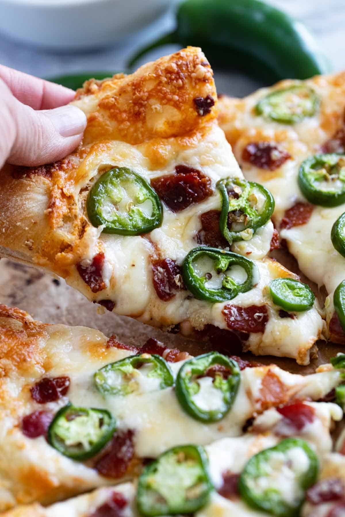 Hand grabbing a slice of Jalapeño Popper Pizza.