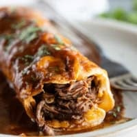Slow Cooker Chile Colorado Burrito on a plate with a bite taken, showing the shredded beef and cheese on the inside.
