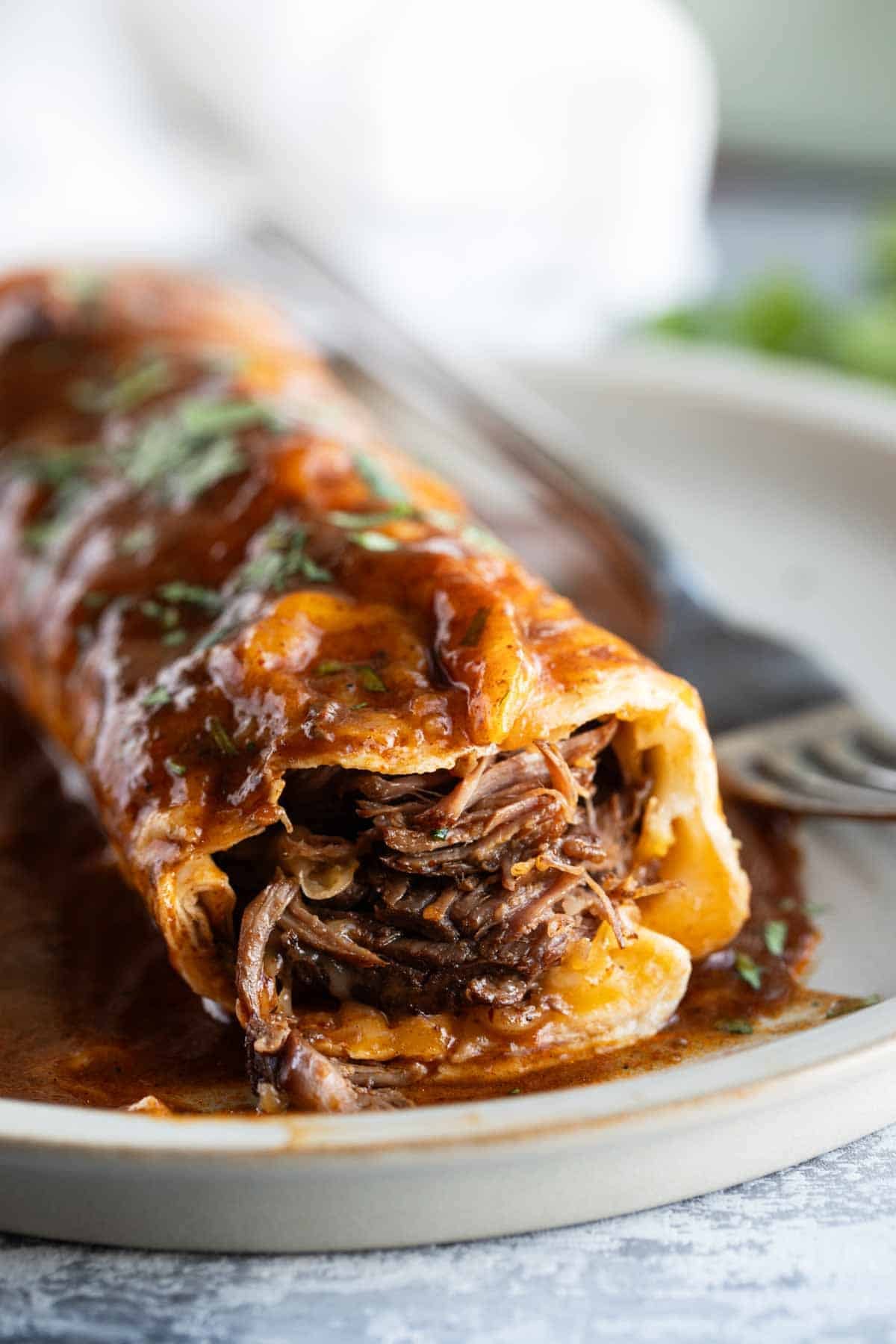 Slow Cooker Chile Colorado Burrito on a plate with a bite taken, showing the shredded beef and cheese on the inside.