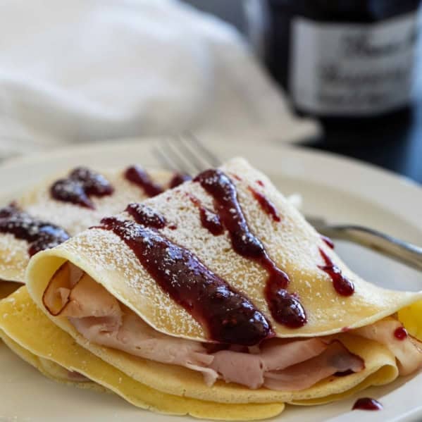 Monte Cristo Crepes with raspberry jam drizzled on top and powdered sugar sprinkled on.