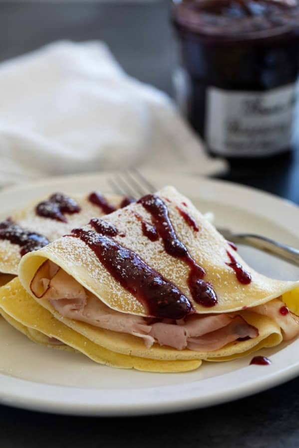 Monte Cristo Crepes with raspberry jam drizzled on top and powdered sugar sprinkled on.