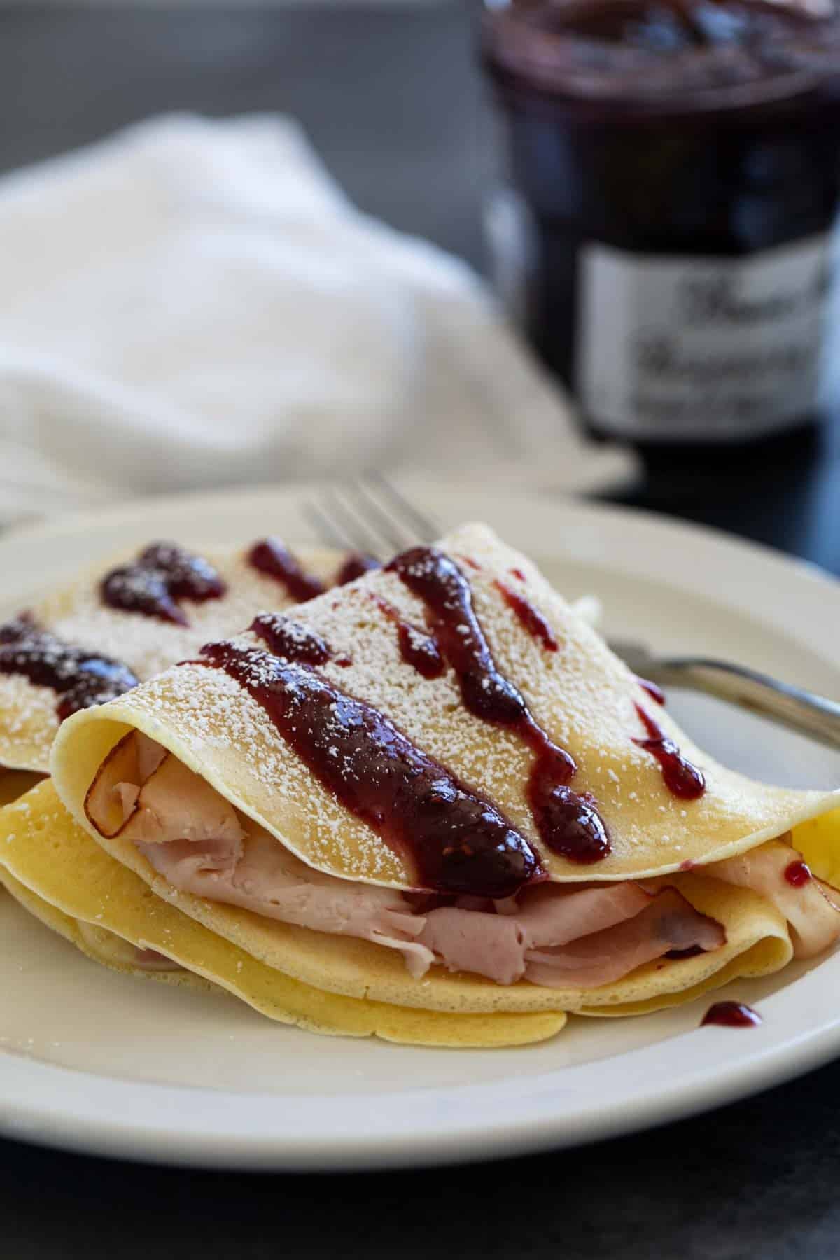 Monte Cristo Crepes with raspberry jam drizzled on top and powdered sugar sprinkled on.