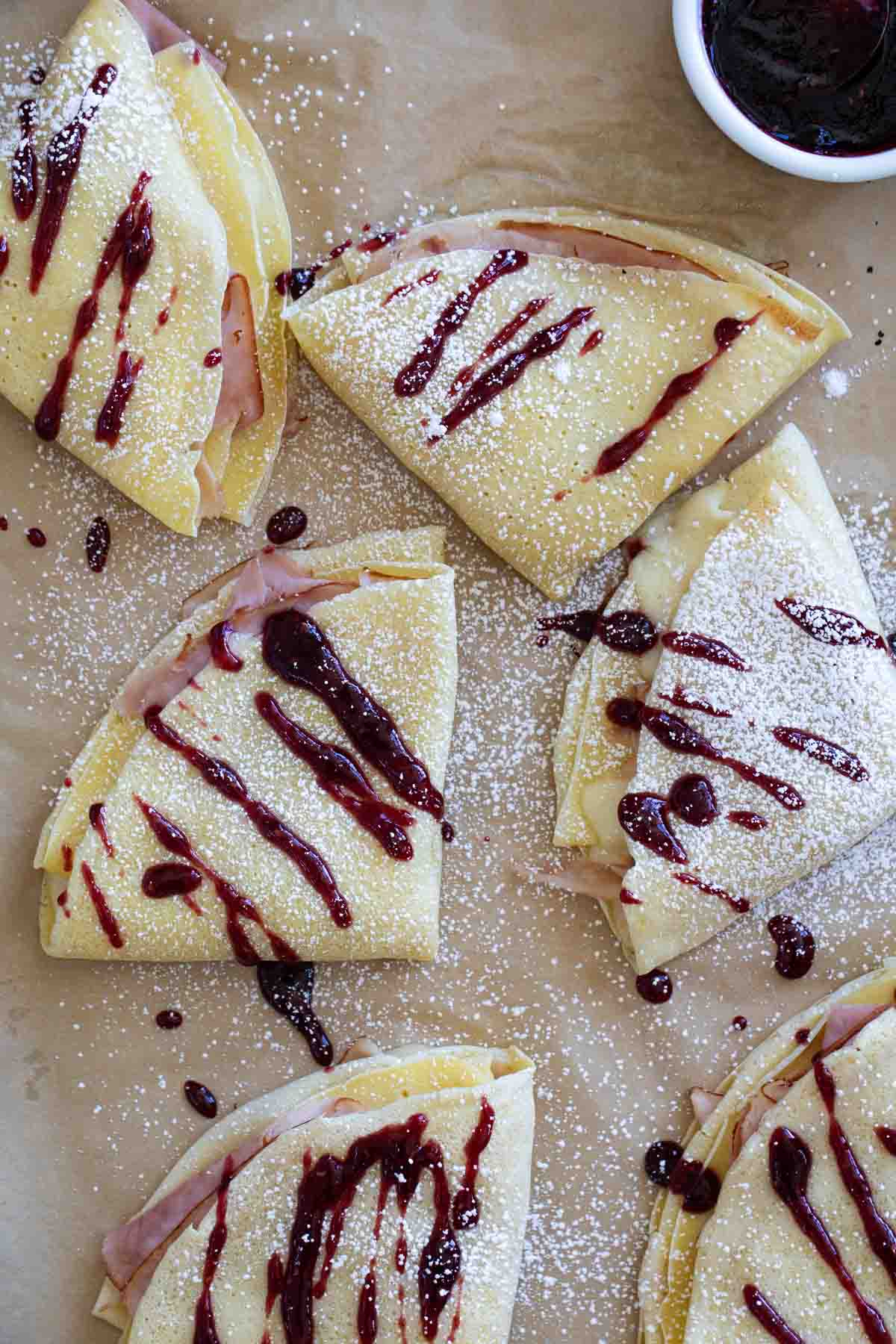 Monte Cristo Crepes topped with raspberry jam and powdered sugar on a baking sheet.