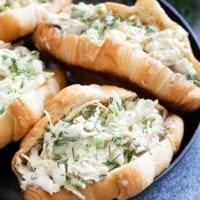 Four pickle chicken salad sandwiches on croissants on a plate.
