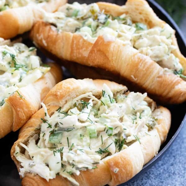 Four pickle chicken salad sandwiches on croissants on a plate.