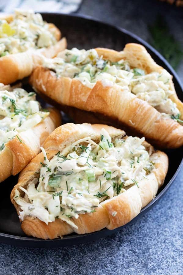 Four pickle chicken salad sandwiches on croissants on a plate.