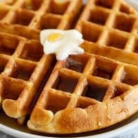 Waffle on a plate topped with butter and syrup.