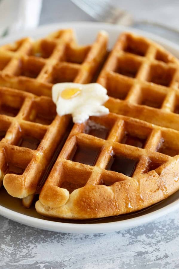 Waffle on a plate topped with butter and syrup.