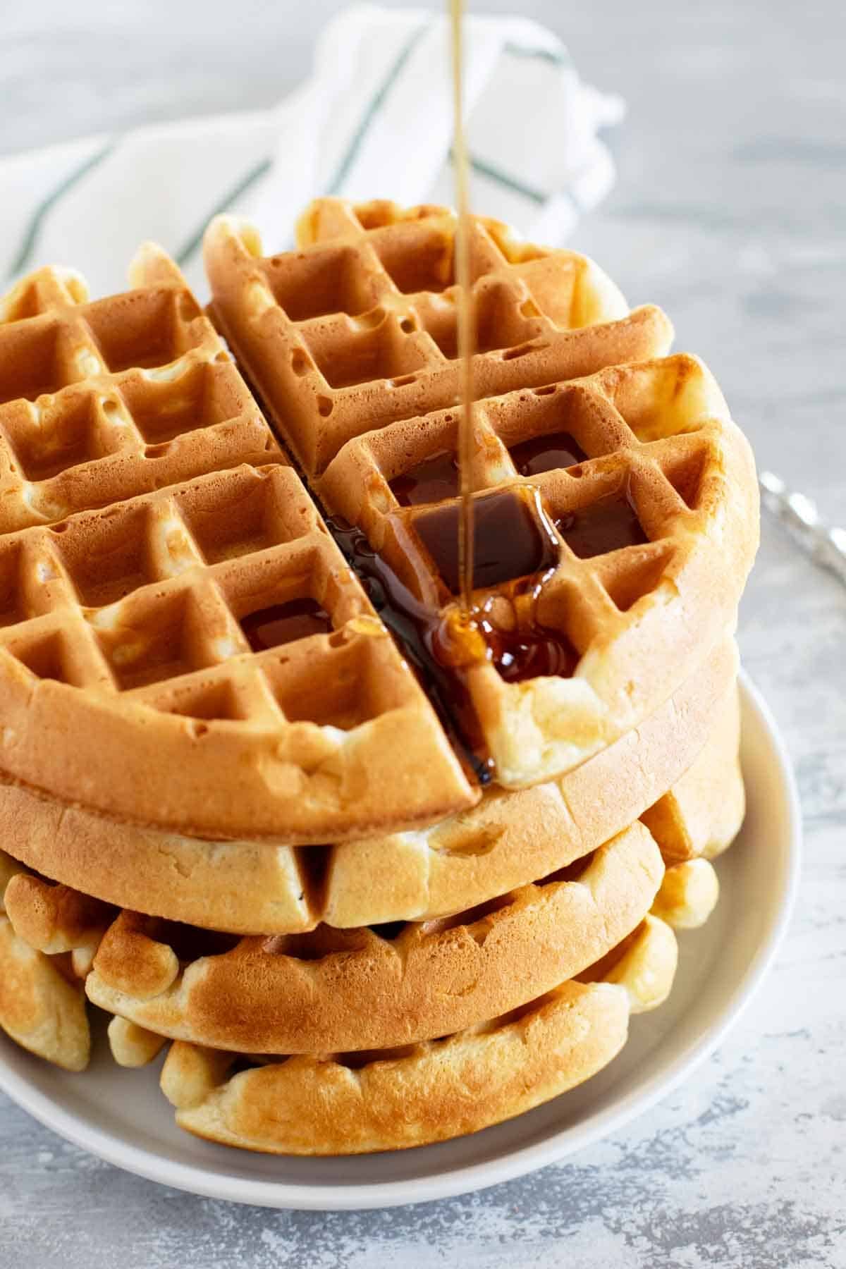Pouring syrup on a stack of homemade waffles.