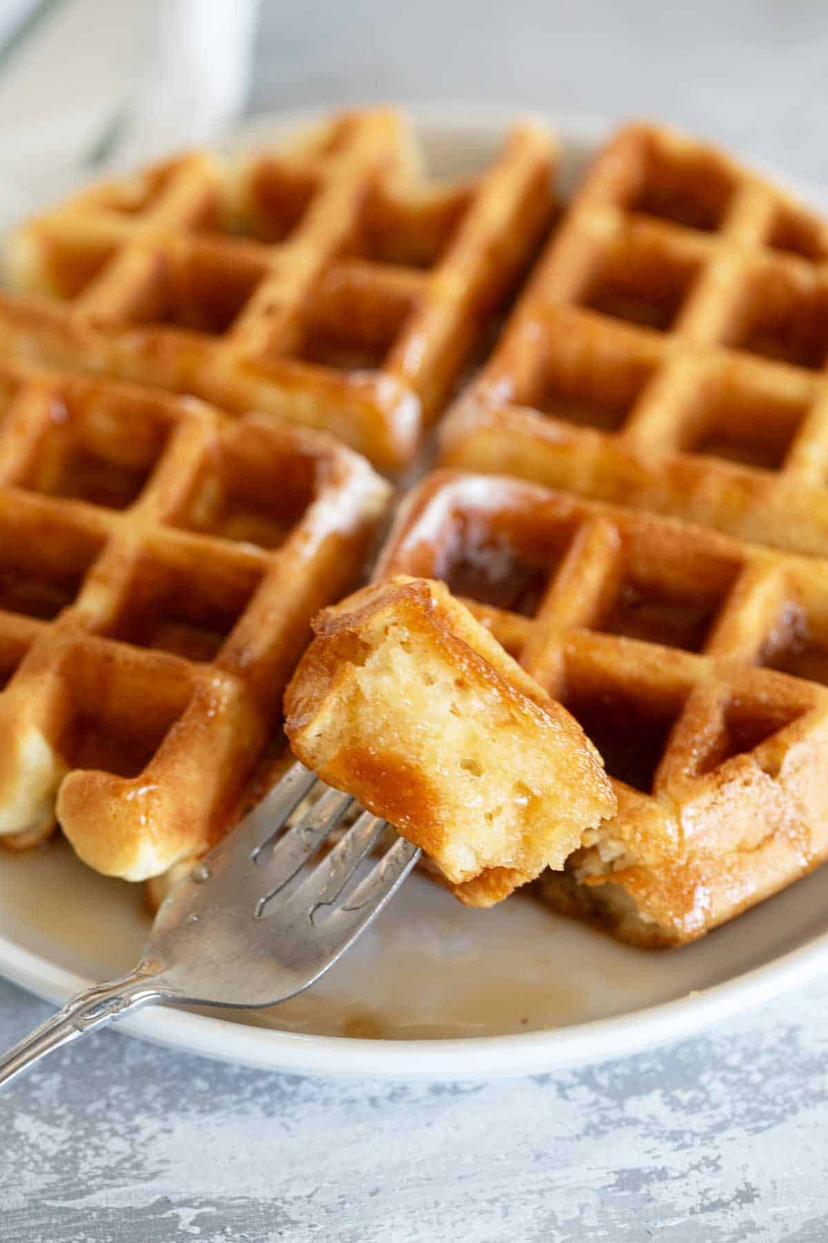 Waffle on a plate with a piece of waffle on a fork.
