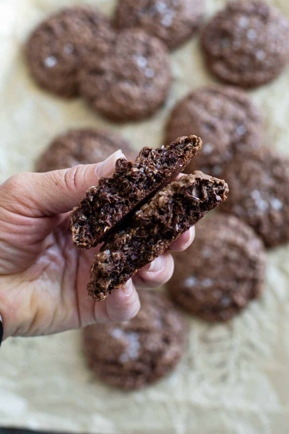 Hand holding a double chocolate oatmeal cookie broken in half.