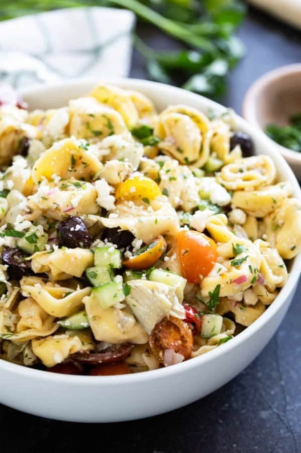 Bowl of Greek Tortellini Pasta Salad with vegetables, feta cheese, and parsley.