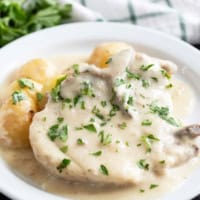 White plate with Slow Cooker Creamy Ranch Pork Chops and Potatoes with parsley sprinkled on top.