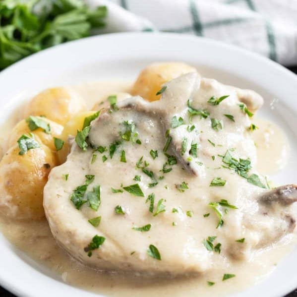 White plate with Slow Cooker Creamy Ranch Pork Chops and Potatoes with parsley sprinkled on top.