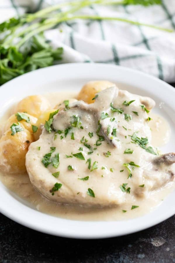 White plate with Slow Cooker Creamy Ranch Pork Chops and Potatoes with parsley sprinkled on top.