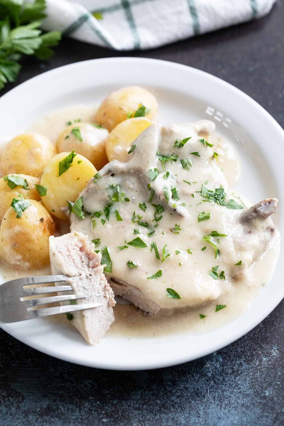 Slow Cooker Creamy Ranch Pork Chops and Potatoes on a plate, with a fork with a bite of pork.