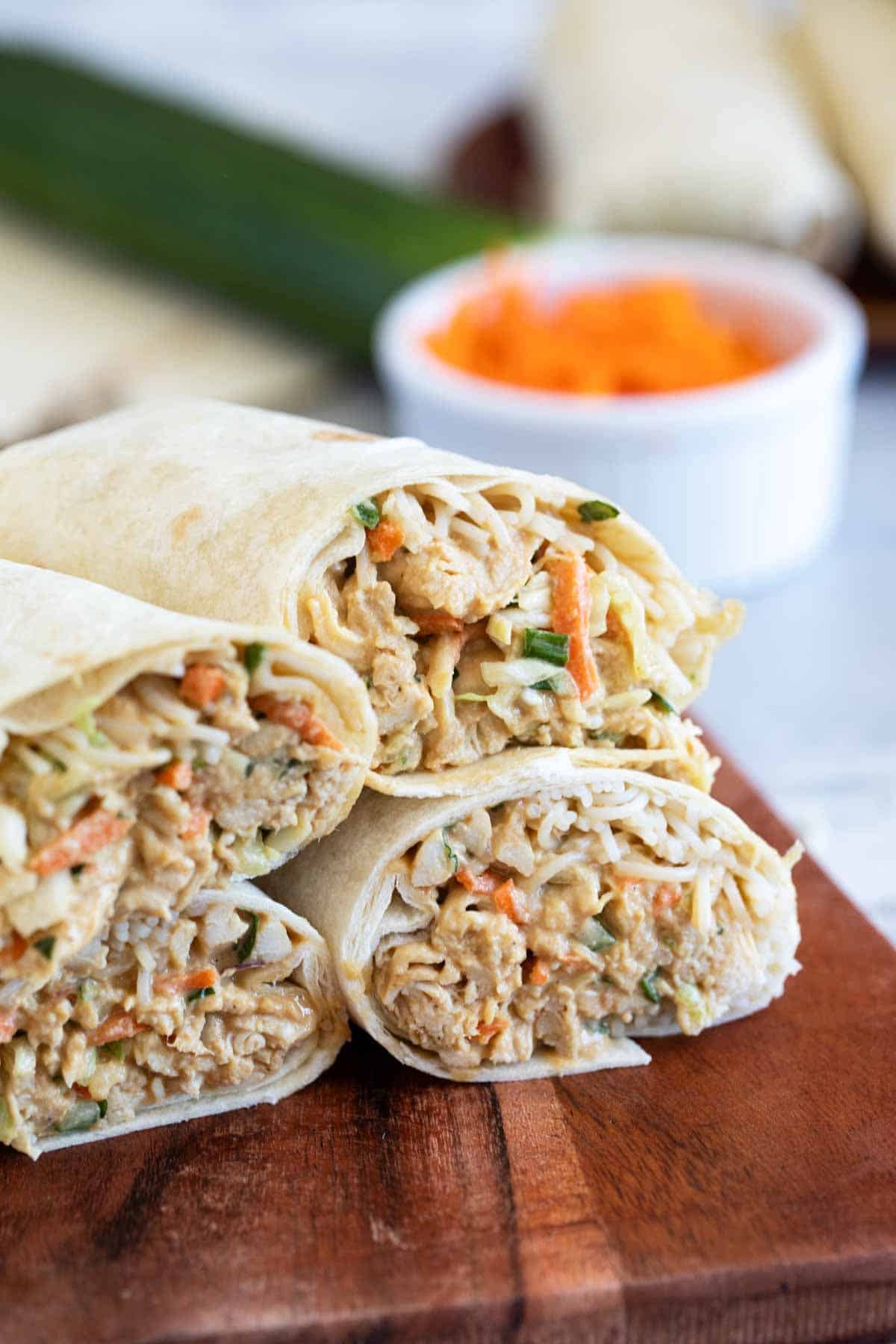 Thai Chicken Wraps cut in half on a wooden cutting board.