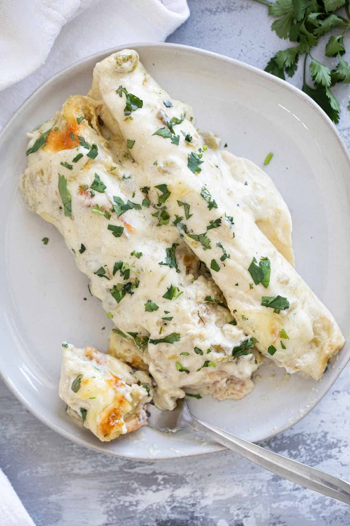 Two White Chicken Enchiladas on a plate with a bite taken from one.