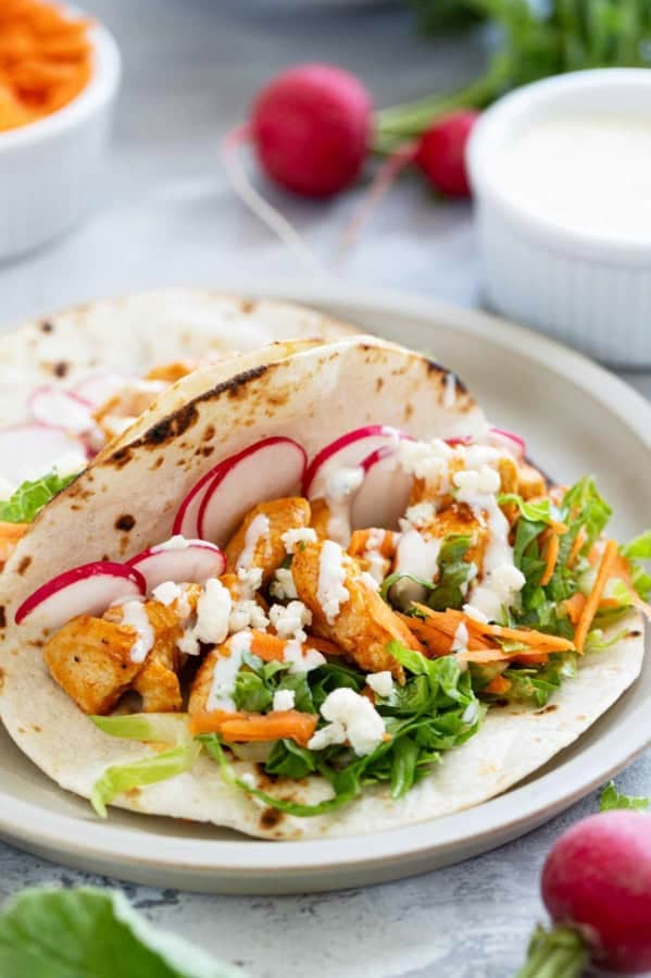 Buffalo Chicken Tacos on flour tortillas, topped with lettuce, carrots, radishes, and blue cheese dressing.