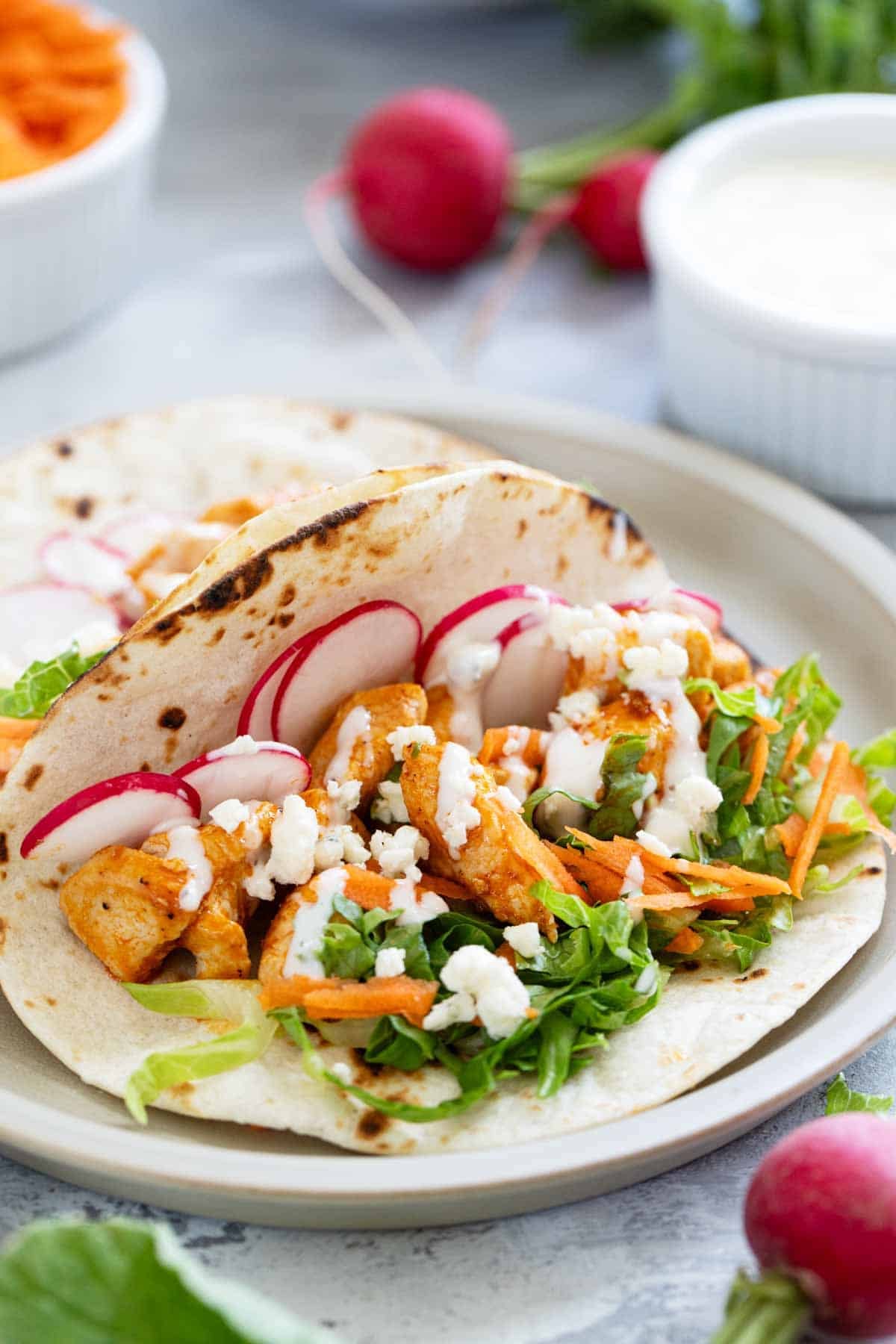 Buffalo Chicken Tacos on flour tortillas, topped with lettuce, carrots, radishes, and blue cheese dressing.