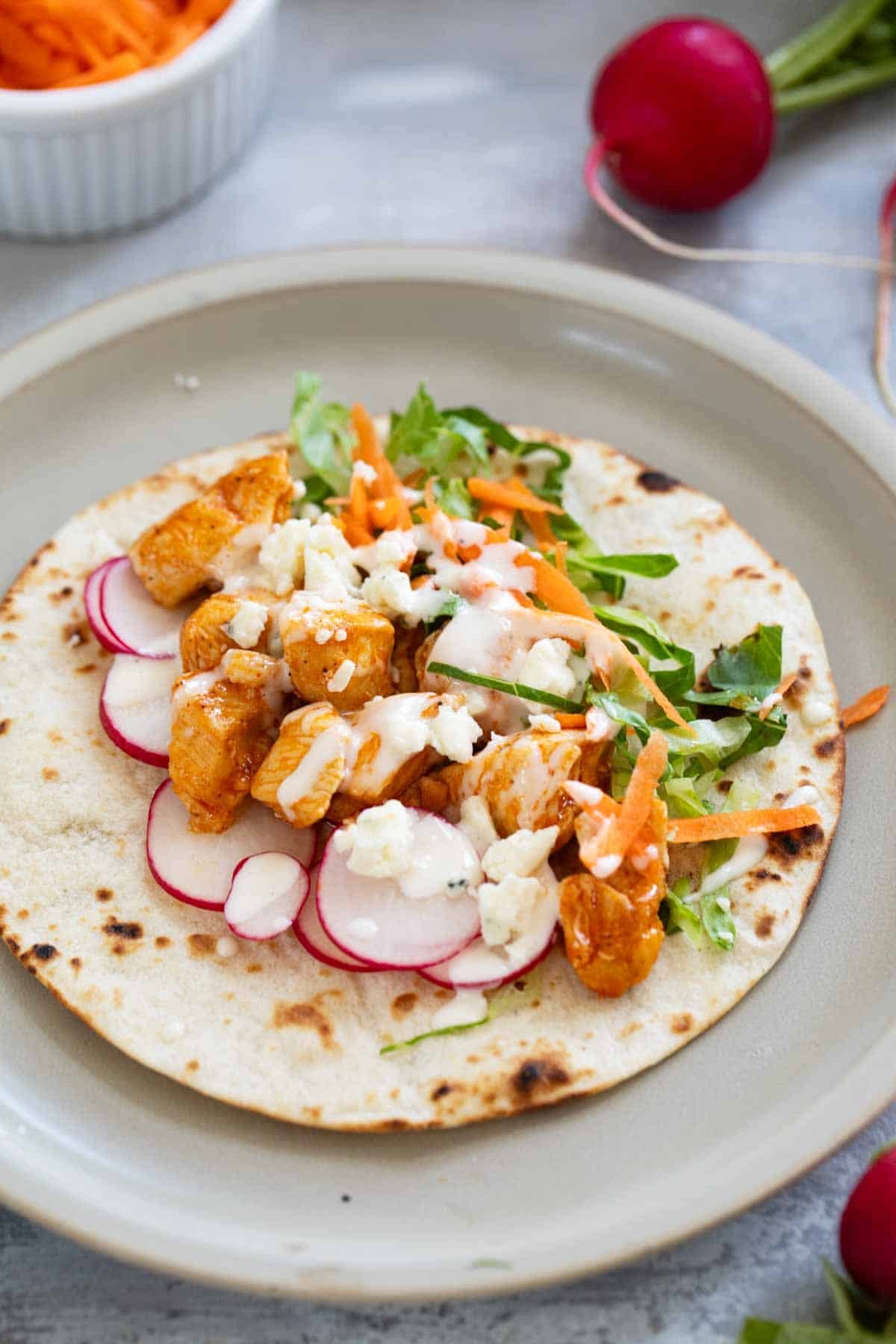 Buffalo Chicken Taco topped with lettuce, radishes, carrots, and blue cheese.