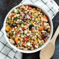 White bowl filled with Mediterranean Bean Salad topped with parsley and feta cheese.