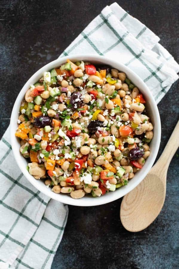 White bowl filled with Mediterranean Bean Salad topped with parsley and feta cheese.