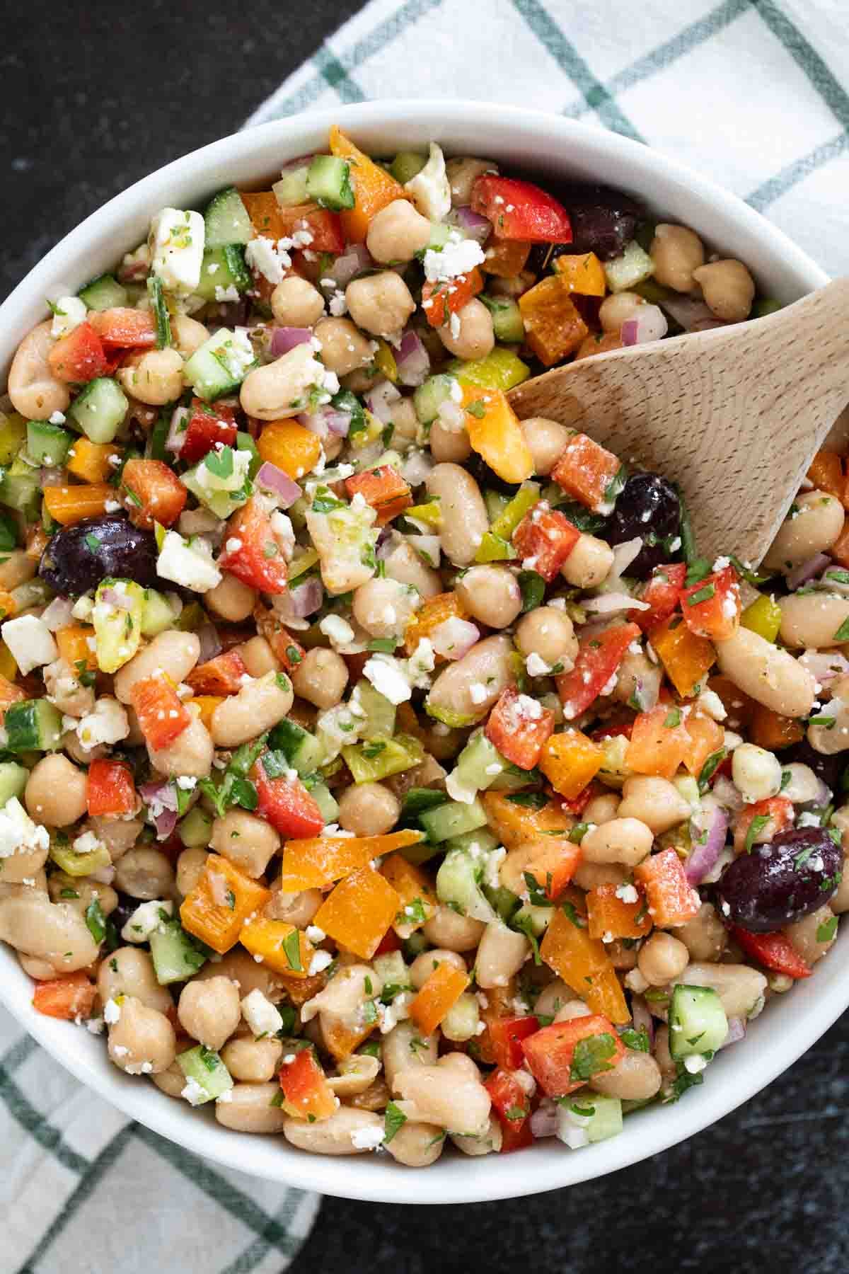 Bowl of Mediterranean Bean Salad with a wooden spoon.