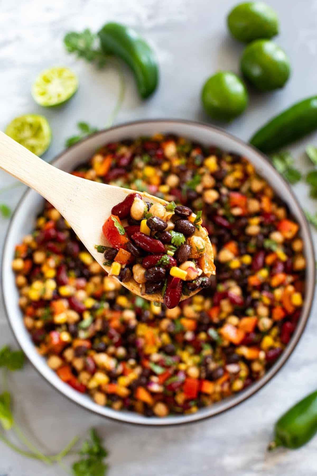 Bowl filled with Mexican bean salad, with a wooden spoon filled with the salad.