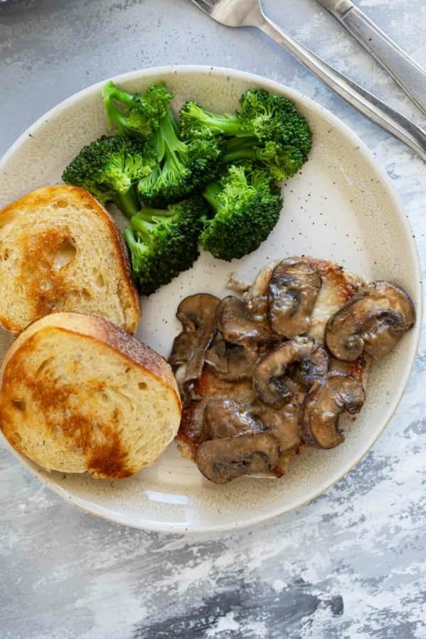 Pork Chop with Dijon Mushrooms on a plate with a fork and side dishes.