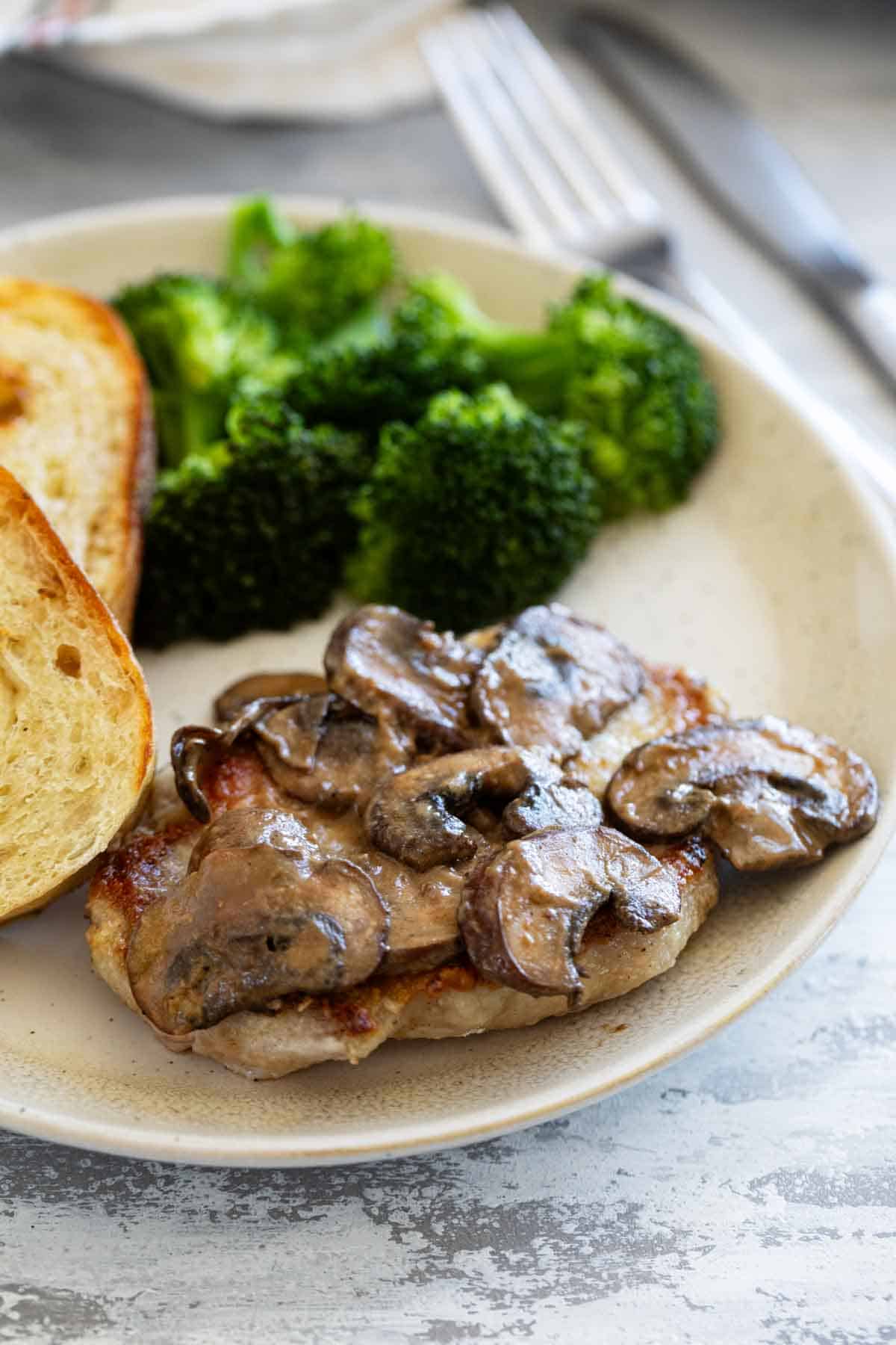 Pork Chop with Dijon Mushrooms on a plate with bread and broccoli.