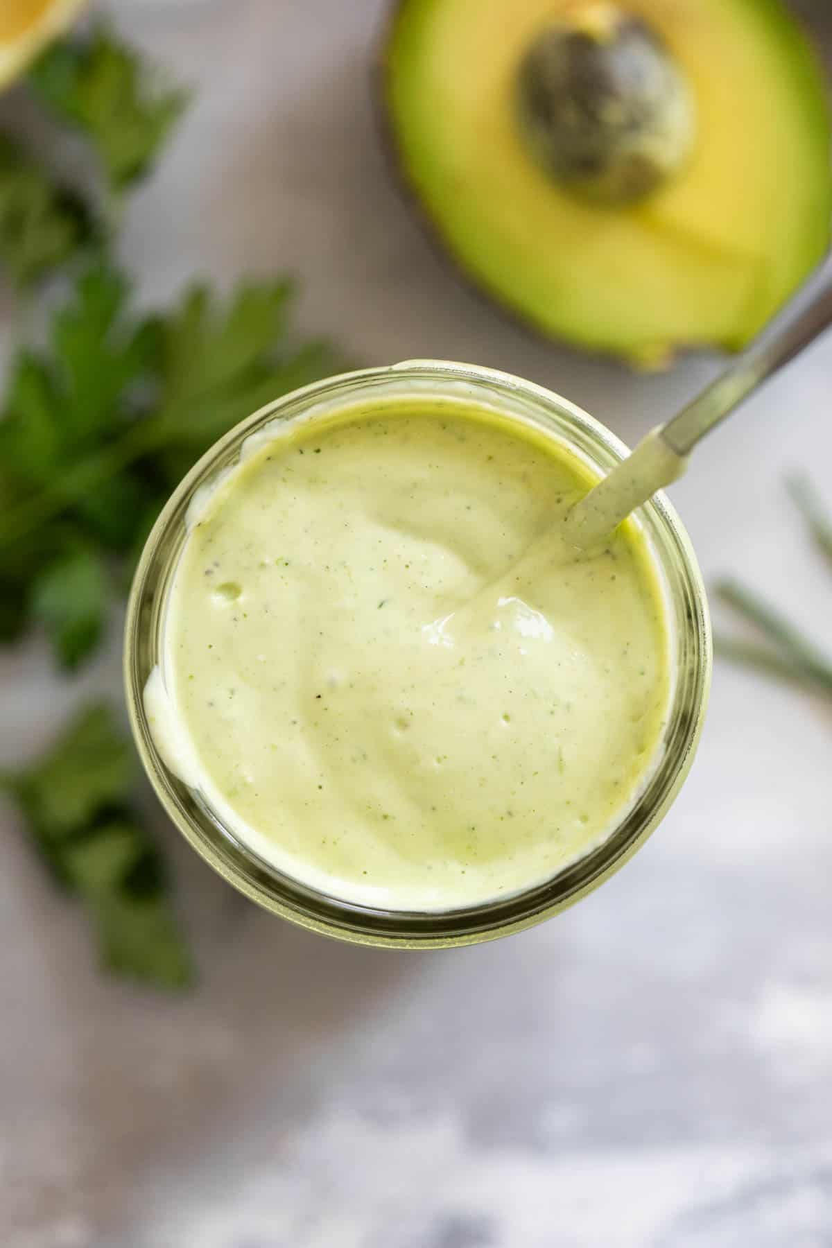 Jar of homemade Avocado Ranch Dressing surrounded by fresh herbs.