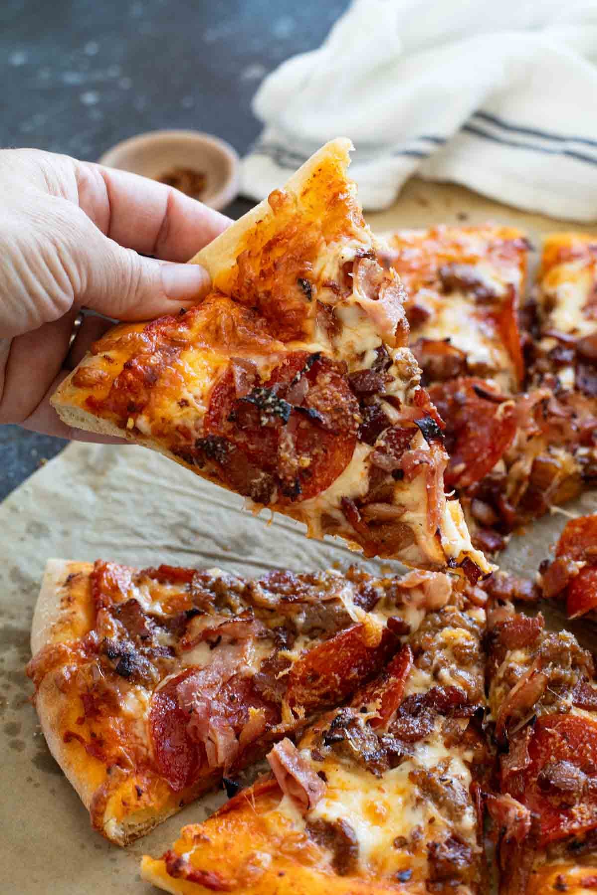 Hand holding a slice of Meat Lover's Pizza.