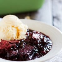 Serving of red velvet cobbler in a white bowl with a scoop of vanilla ice cream on top.