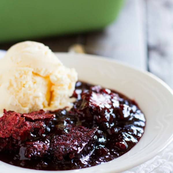 Serving of red velvet cobbler in a white bowl with a scoop of vanilla ice cream on top.