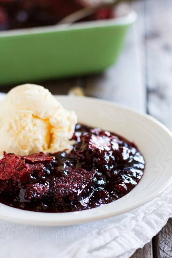 Serving of red velvet cobbler in a white bowl with a scoop of vanilla ice cream on top.