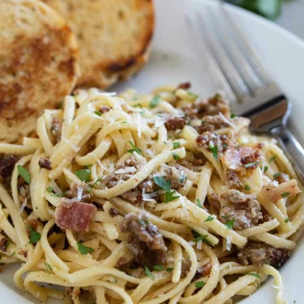 Sausage Carbonara Pasta with bacon on a plate served with toasted bread.