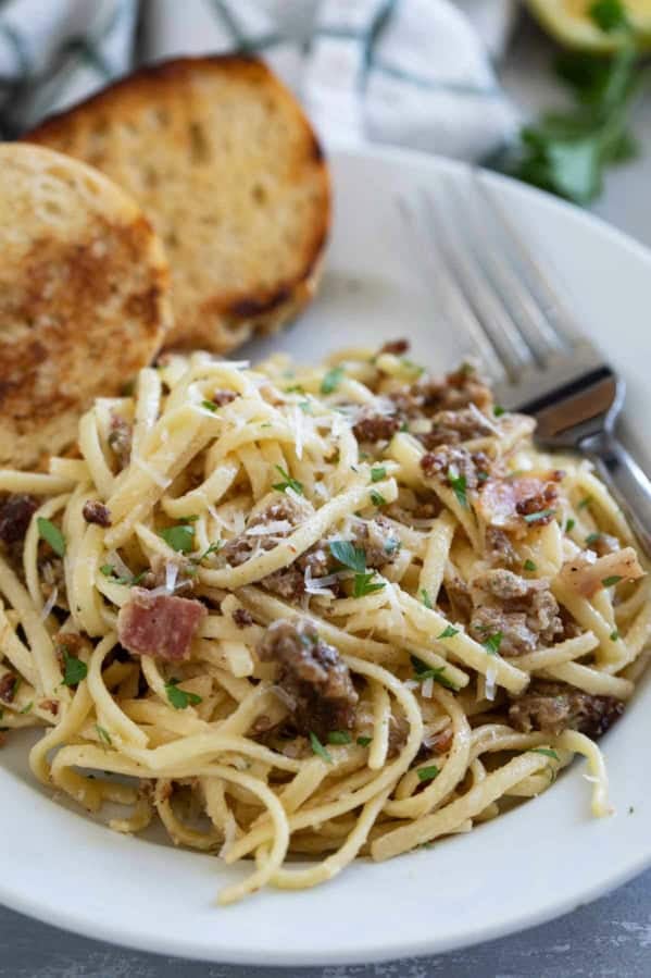 Sausage Carbonara Pasta with bacon on a plate served with toasted bread.