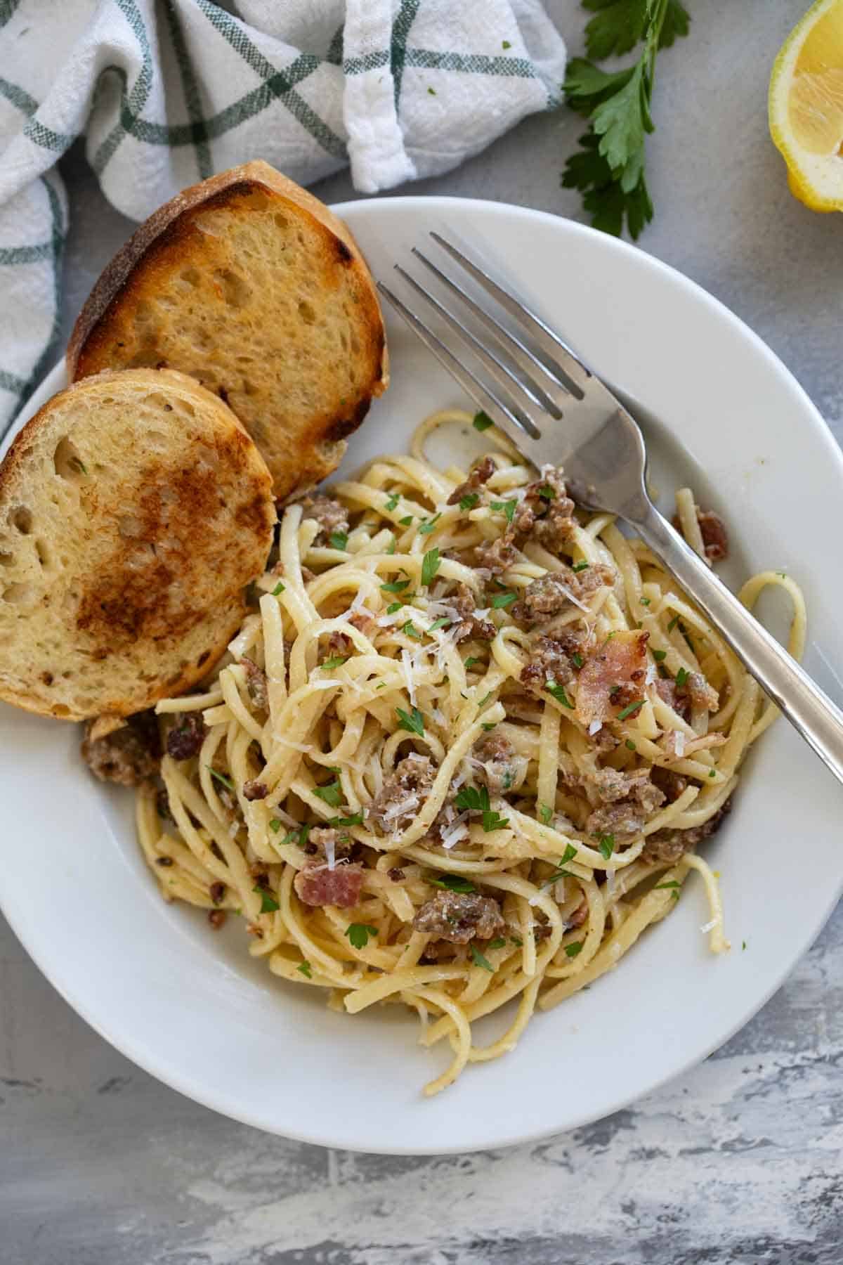 Sausage Carbonara Pasta with bacon in a white dish with toasted bread.