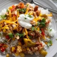 Slow Cooker Tex-Mex Chicken over rice, topped with cheese, sour cream, and cilantro.
