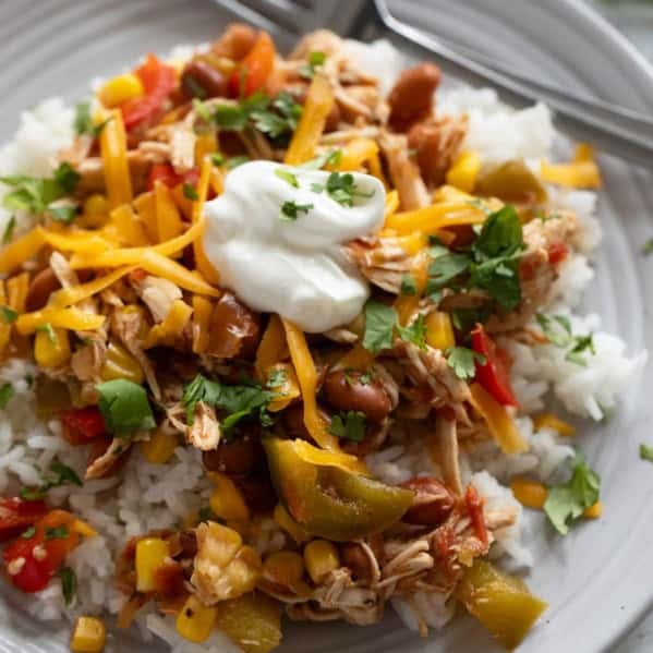Slow Cooker Tex-Mex Chicken over rice, topped with cheese, sour cream, and cilantro.