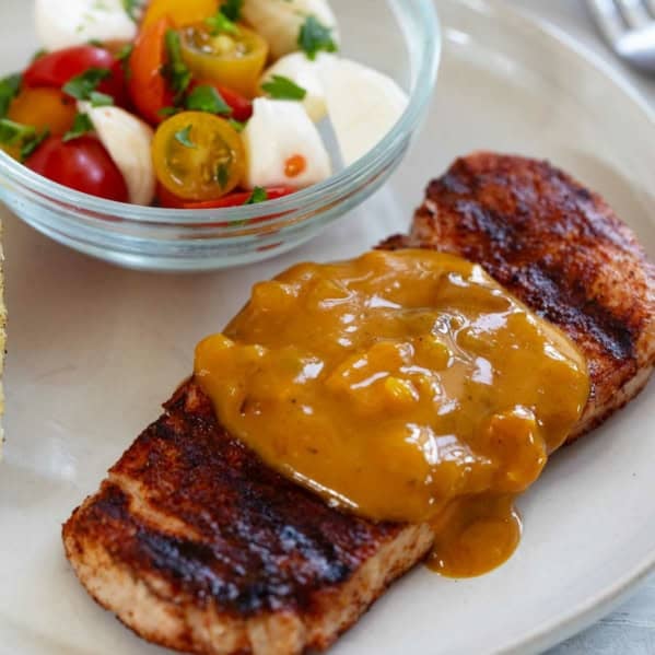 Serving of Spice-Rubbed Pork Chops with Bacon Mustard BBQ Sauce on a plate, with tomatoes on the side.