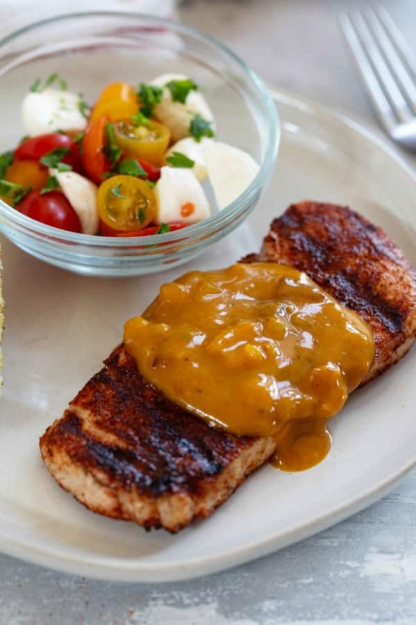 Serving of Spice-Rubbed Pork Chops with Bacon Mustard BBQ Sauce on a plate, with tomatoes on the side.