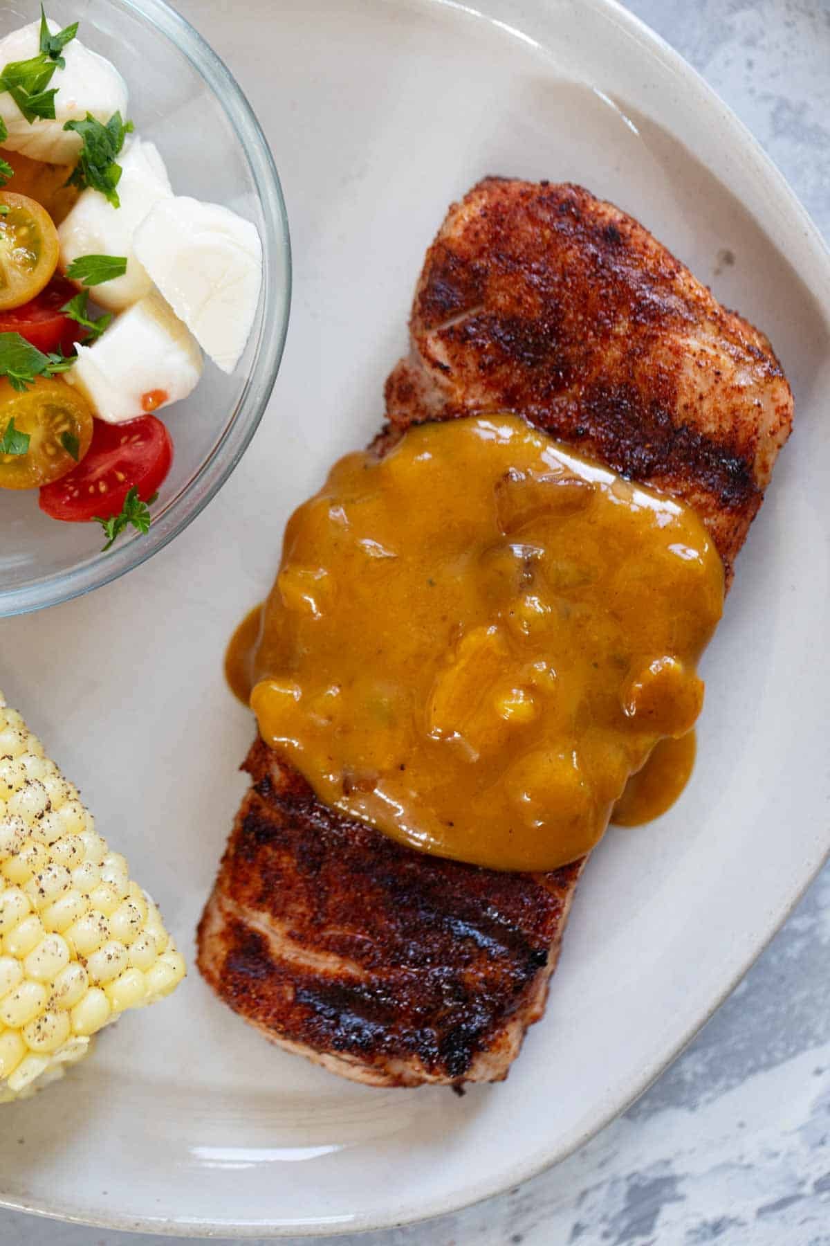 Spice-Rubbed Pork Chop on a plate, topped with Bacon Mustard BBQ Sauce.