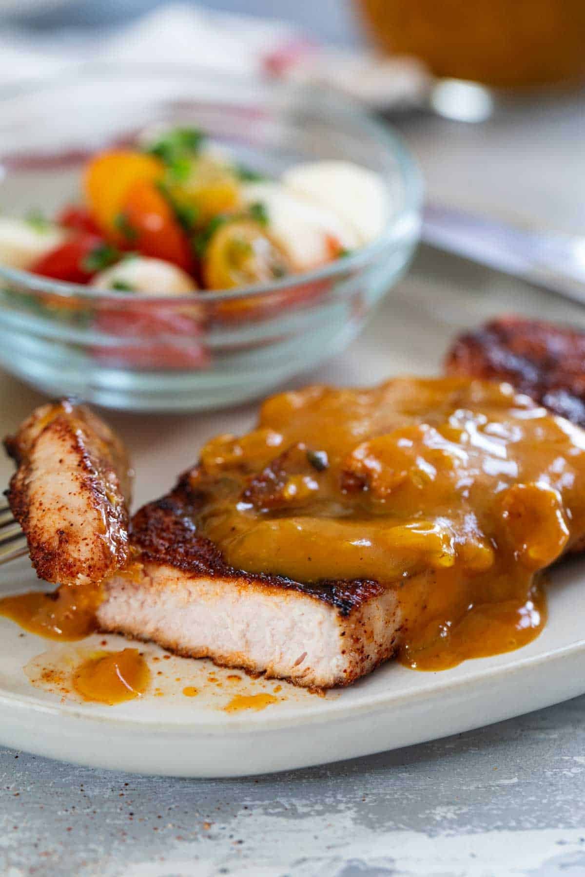 Spice-Rubbed Pork Chops topped with Bacon Mustard BBQ Sauce, with a bite taken from the pork chop.