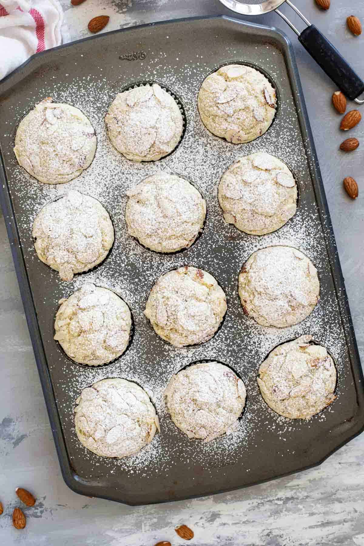 Almond Poppy Seed Muffins in a tin, sprinkled with powdered sugar.